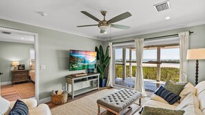 A spacious living room with a large flat-screen TV, a ceiling fan, and a view of the ocean through large windows. - Bayfront Boca Grande North 43 - Top Floor - 2/2 Great Water Views! (Placida)