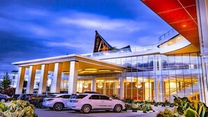 A modern hotel with a glass facade, a prominent entrance with a covered area, and a distinctive roof design. - Labersa Hotel & Convention Centre Toba (Balige)