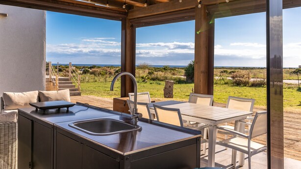 Une cuisine extérieure moderne, dotée d’un évier et d’un espace repas, offrant une vue sur un paysage verdoyant.