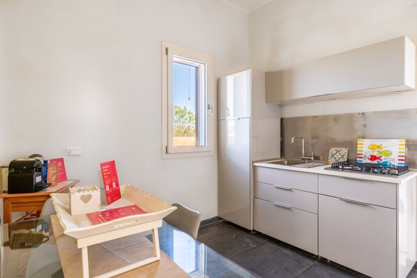 A compact kitchen with a refrigerator, a gas stove, and a sink. There is a small table with a chair, and a window providing natural light. - Casa Faro del Plemmiro con Jacuzzi (Syracuse)