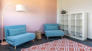 Une pièce avec deux canapés bleus, un lampadaire, un tapis à motifs et une étagère blanche.