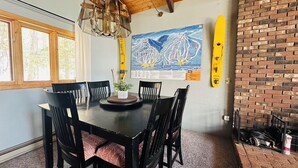 Un coin repas avec une table et des chaises en bois, un lustre, une carte accrochée au mur et un mur en briques.