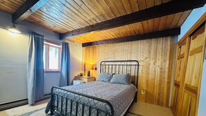 Une chambre à coucher avec un plafond en bois, un lit avec un cadre en métal, une table de chevet et une fenêtre avec des rideaux.
