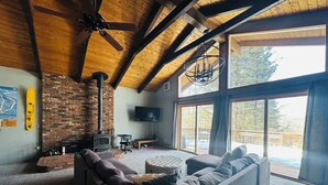 Un salon chaleureux avec une cheminée en briques, une grande fenêtre et un ventilateur de plafond.