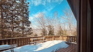 Une terrasse en bois avec une rambarde, des bancs et de la neige au sol.