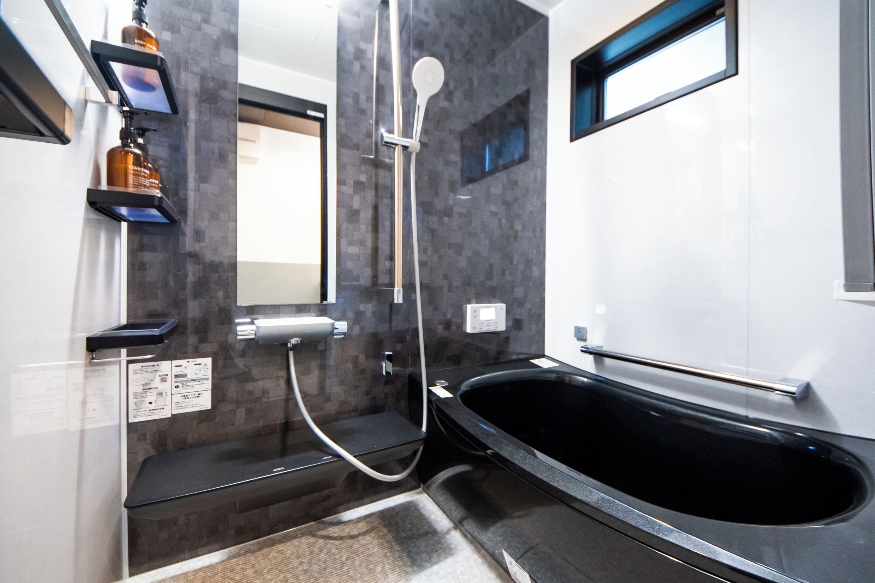 Een moderne badkamer met een zwart bad, een douche met glazen wanden en een digitaal bedieningspaneel.
