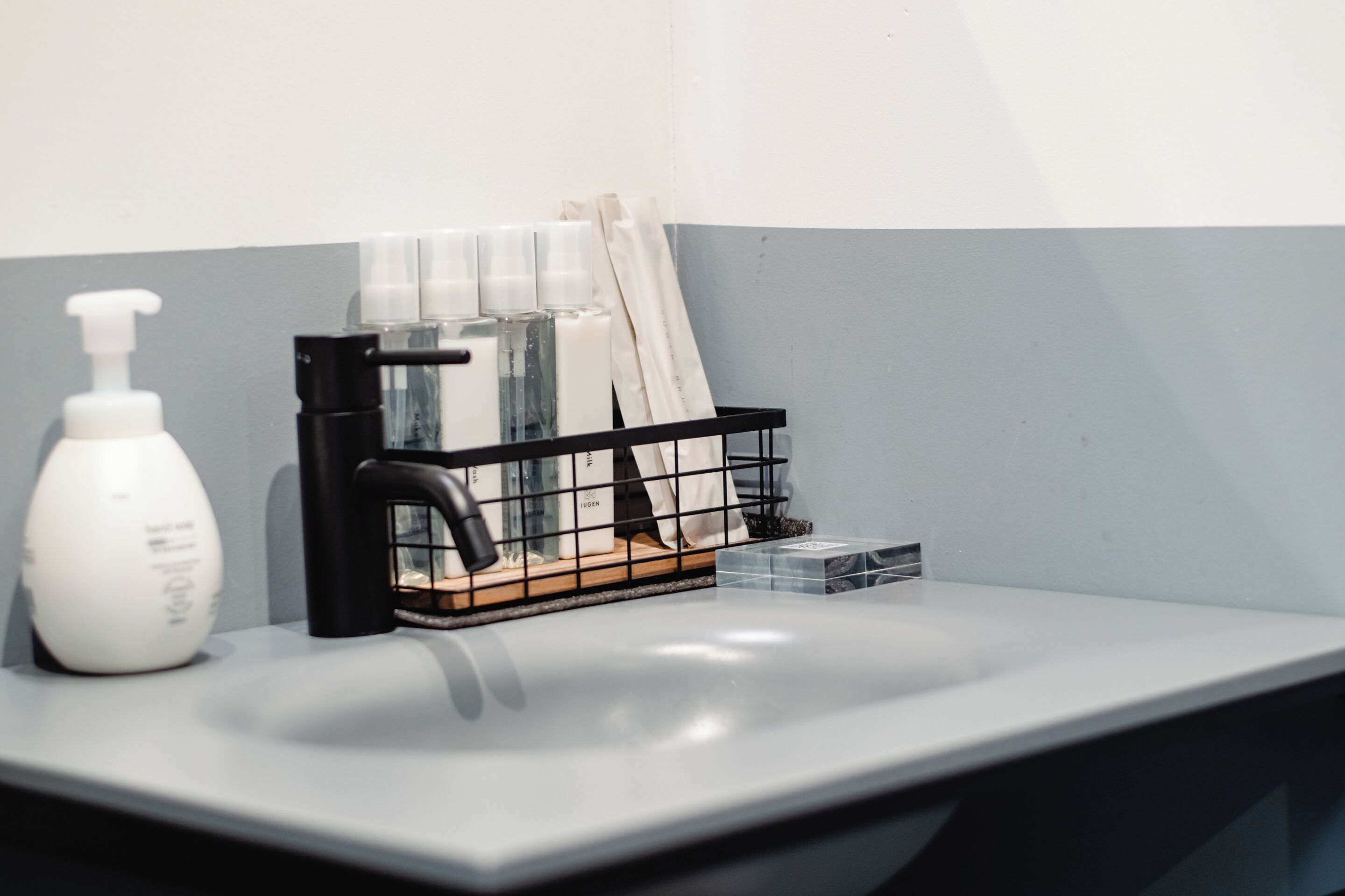 A bathroom sink with a soap dispenser, a black soap holder, and a glass container.