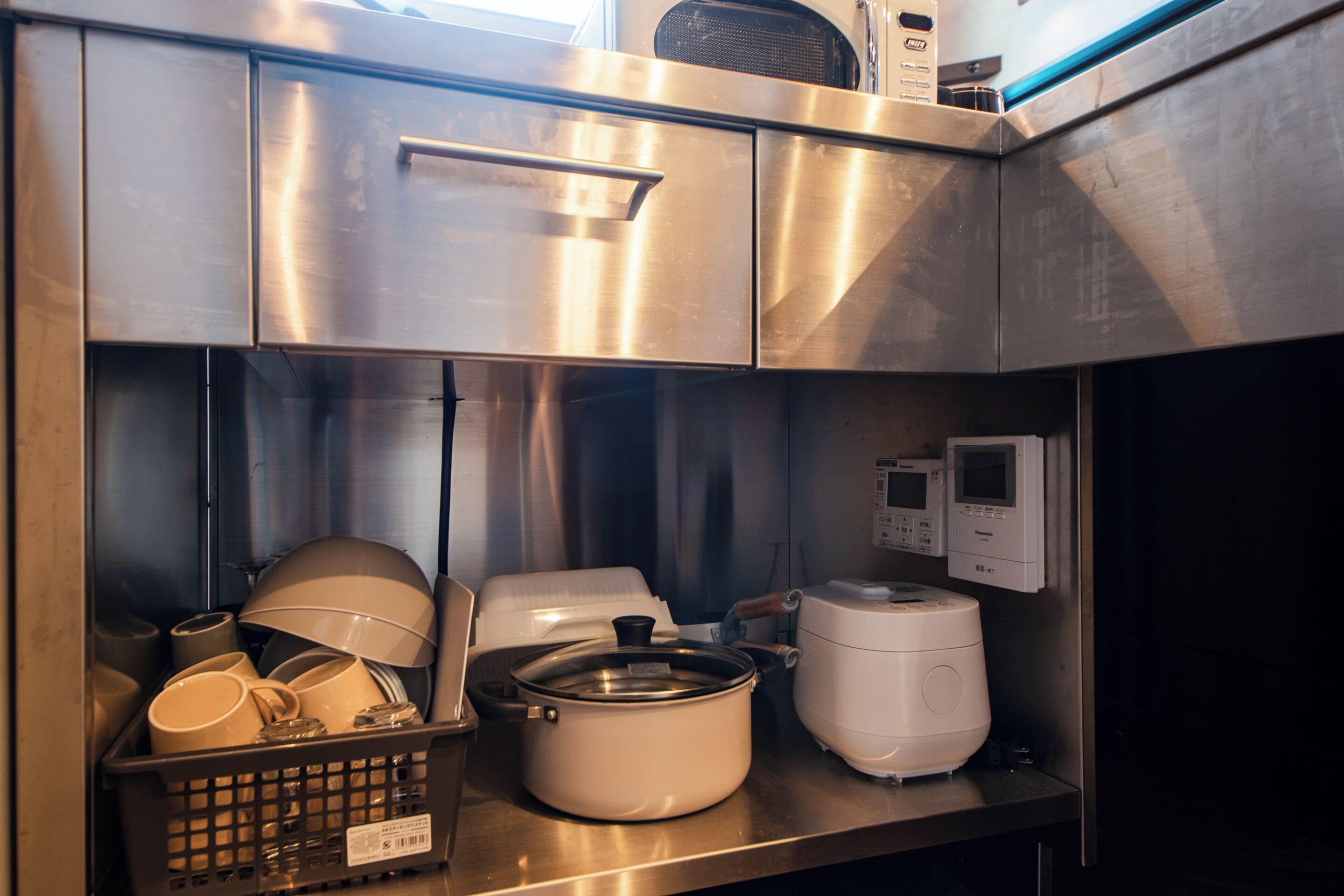 Une cuisine en acier inoxydable équipée d’un four à micro-ondes, d’un cuiseur à riz et d’un égouttoir à vaisselle.