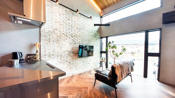 A modern kitchen with a brick wall, a large window, and a wooden ceiling. - Private House Hibiki (Nara)