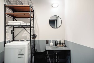 Una habitación de hotel compacta con lavadora y secadora integradas, un lavamanos pequeño con artículos de aseo y un espejo en la pared.