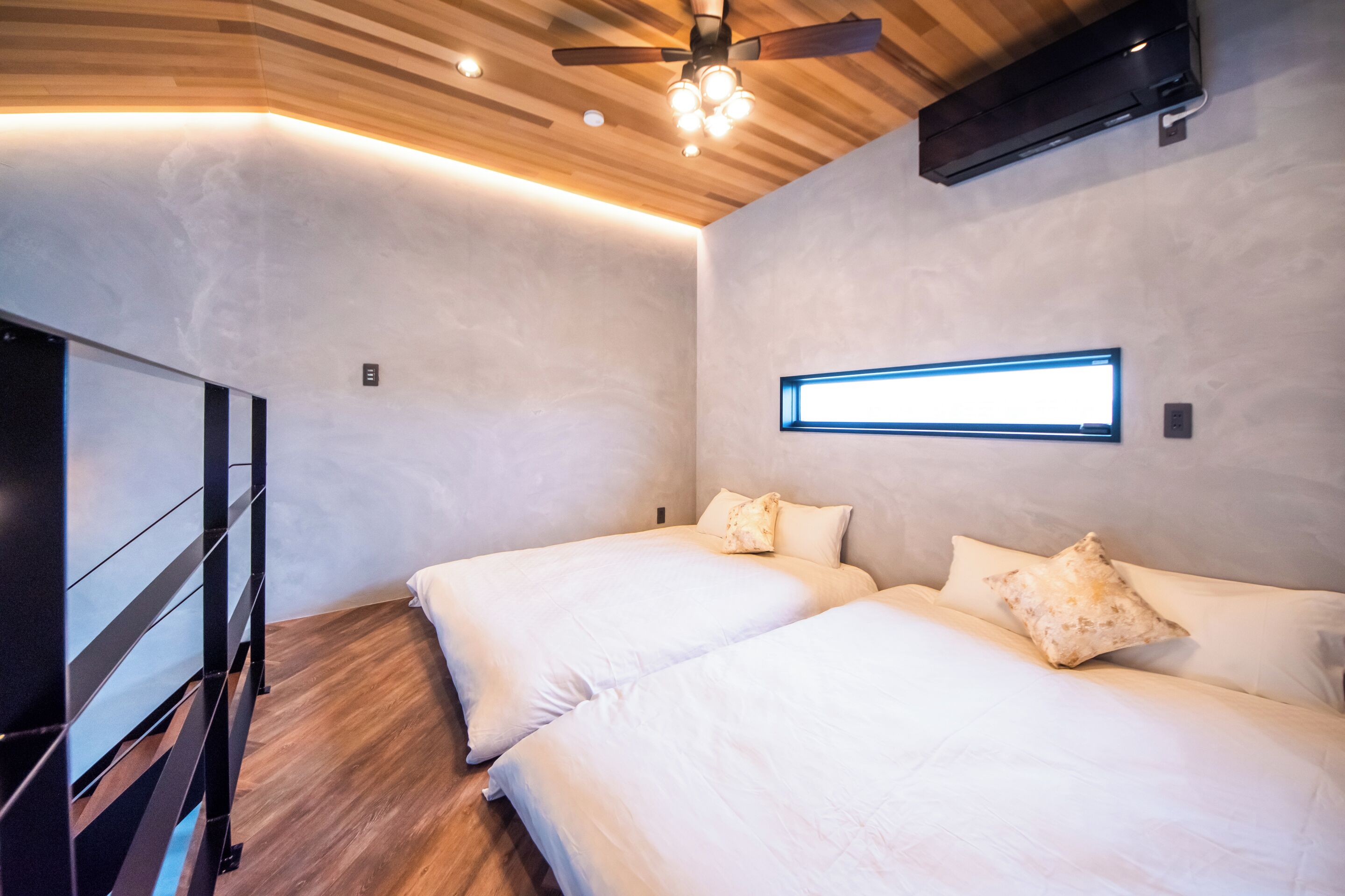 Une chambre avec deux lits, un ventilateur de plafond, des spots encastrés et une fenêtre.