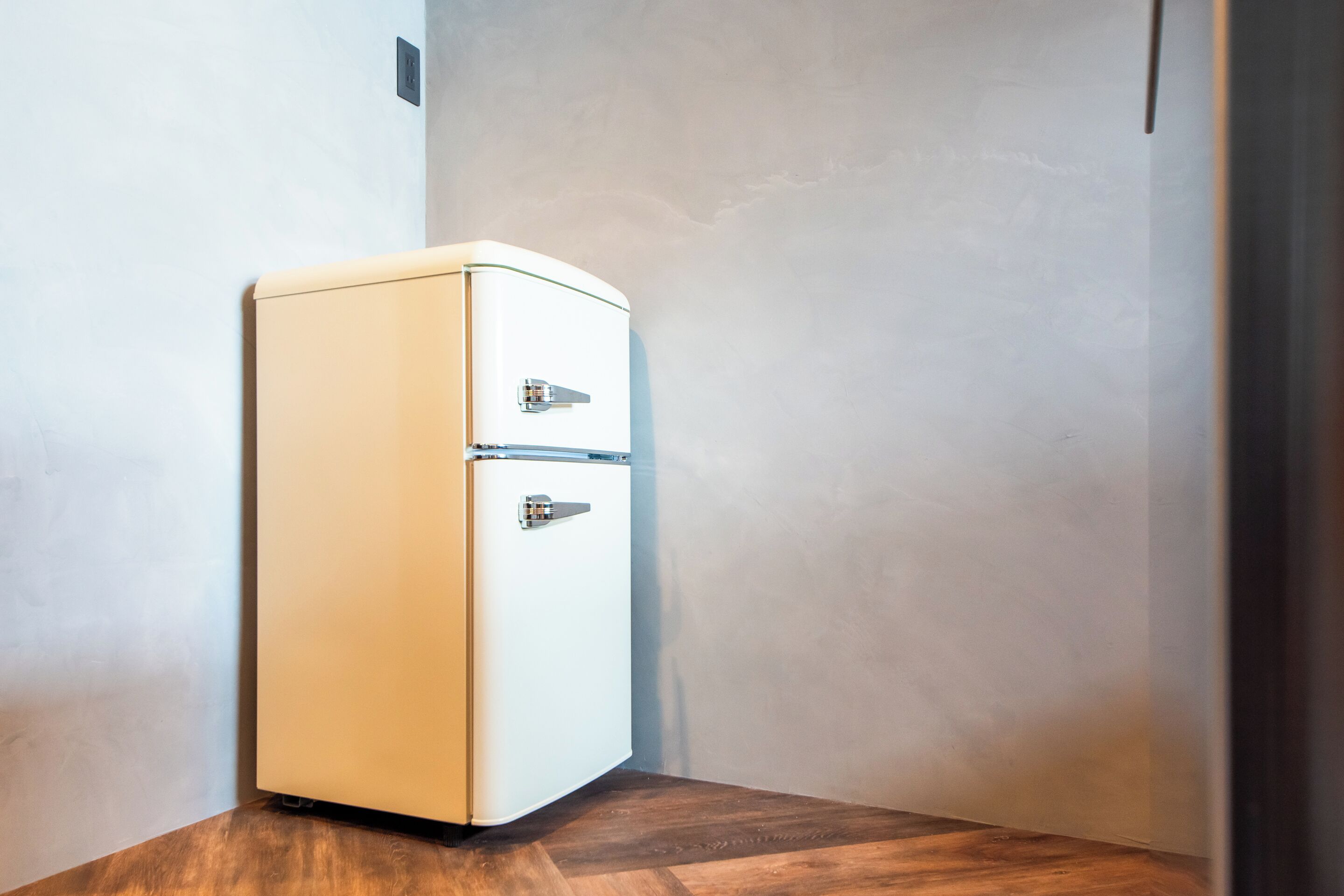 A corner of a room with a white refrigerator and a wooden floor.