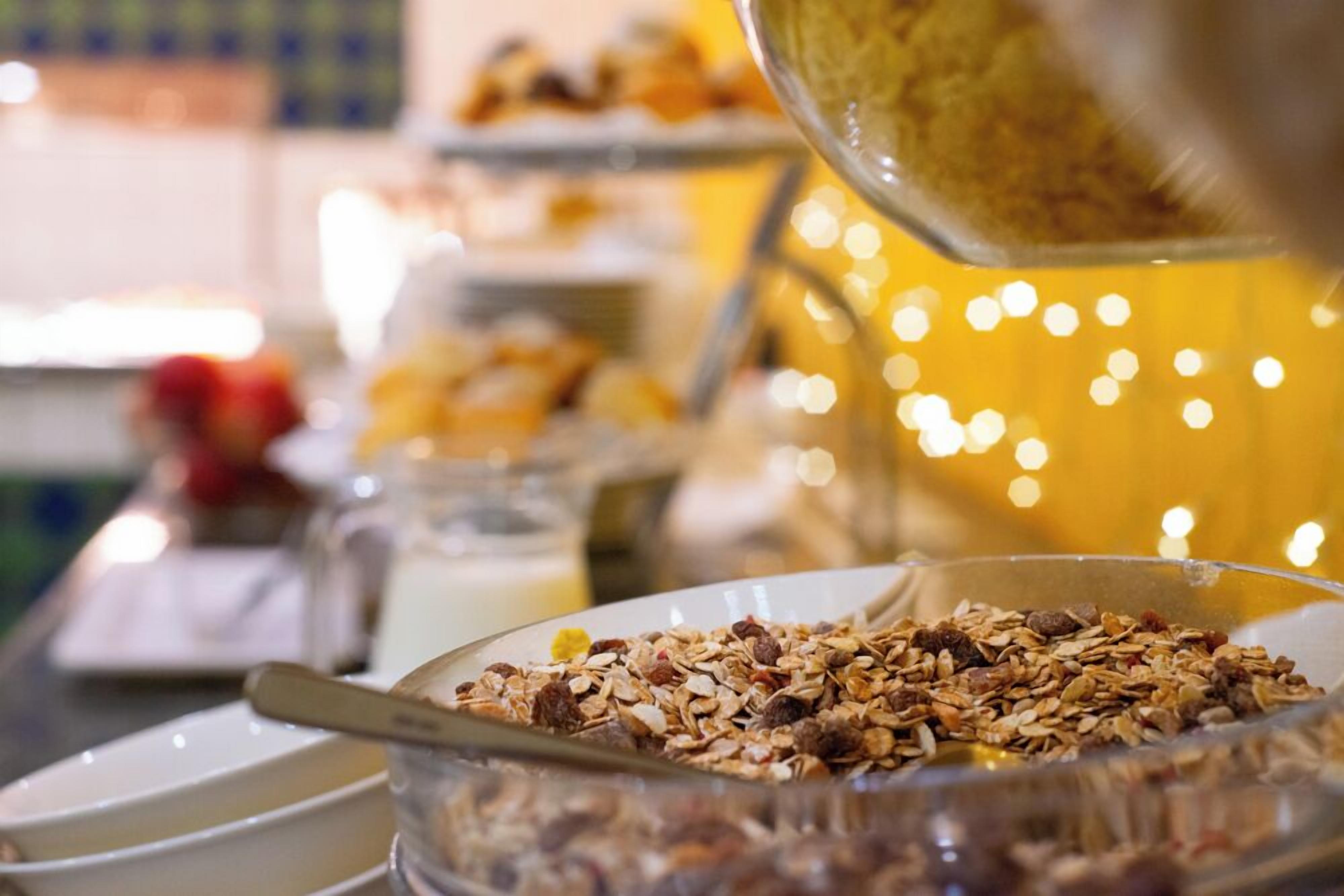 A breakfast buffet with various food items and a glass bowl filled with granola.