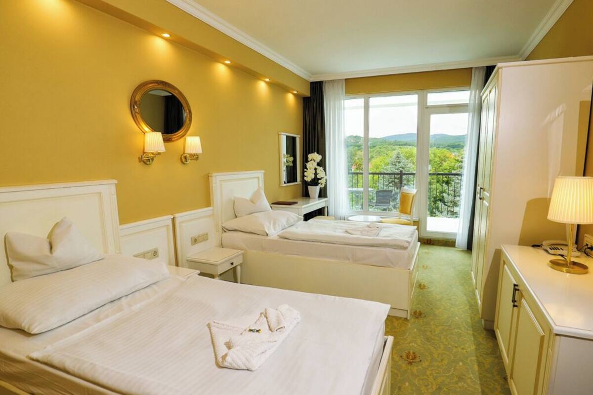Quarto de hotel com duas camas, varanda e vista, e uma secretária com candeeiro.