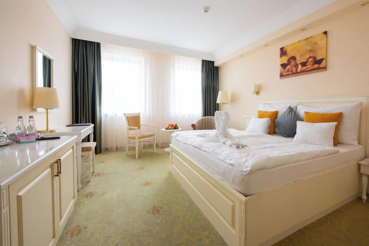 Quarto de hotel com cama, escrivaninha, cadeira, mesa de cabeceira e um quadro na parede.