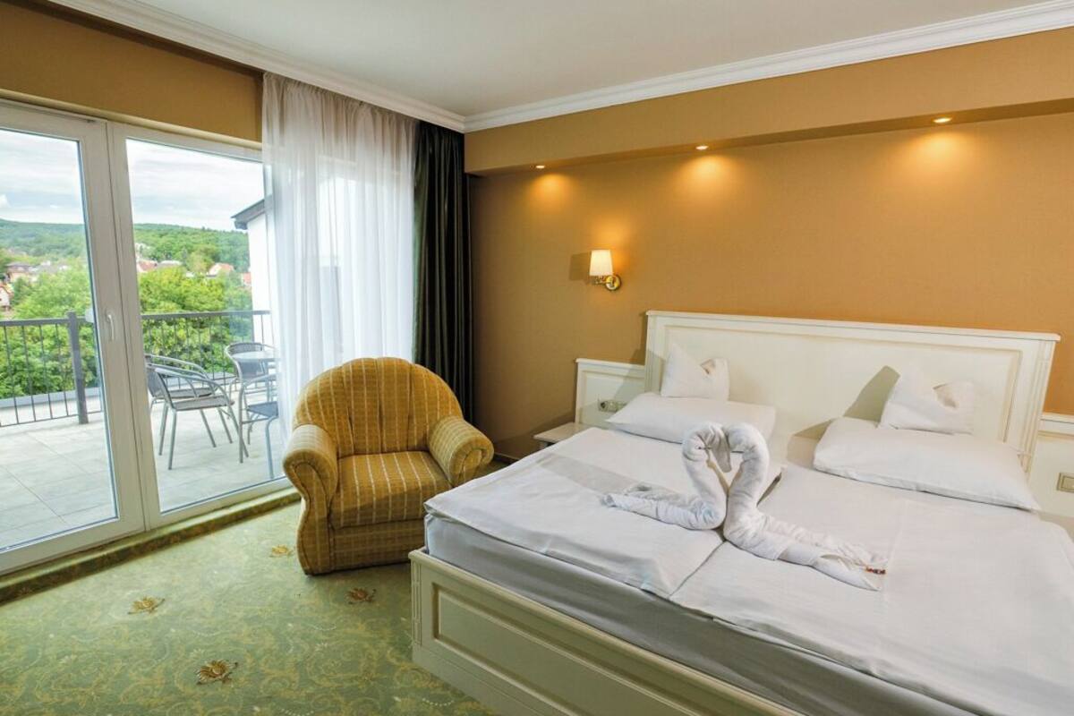 Quarto de hotel com cama, cadeira, mesa de cabeceira e vista para o exterior.