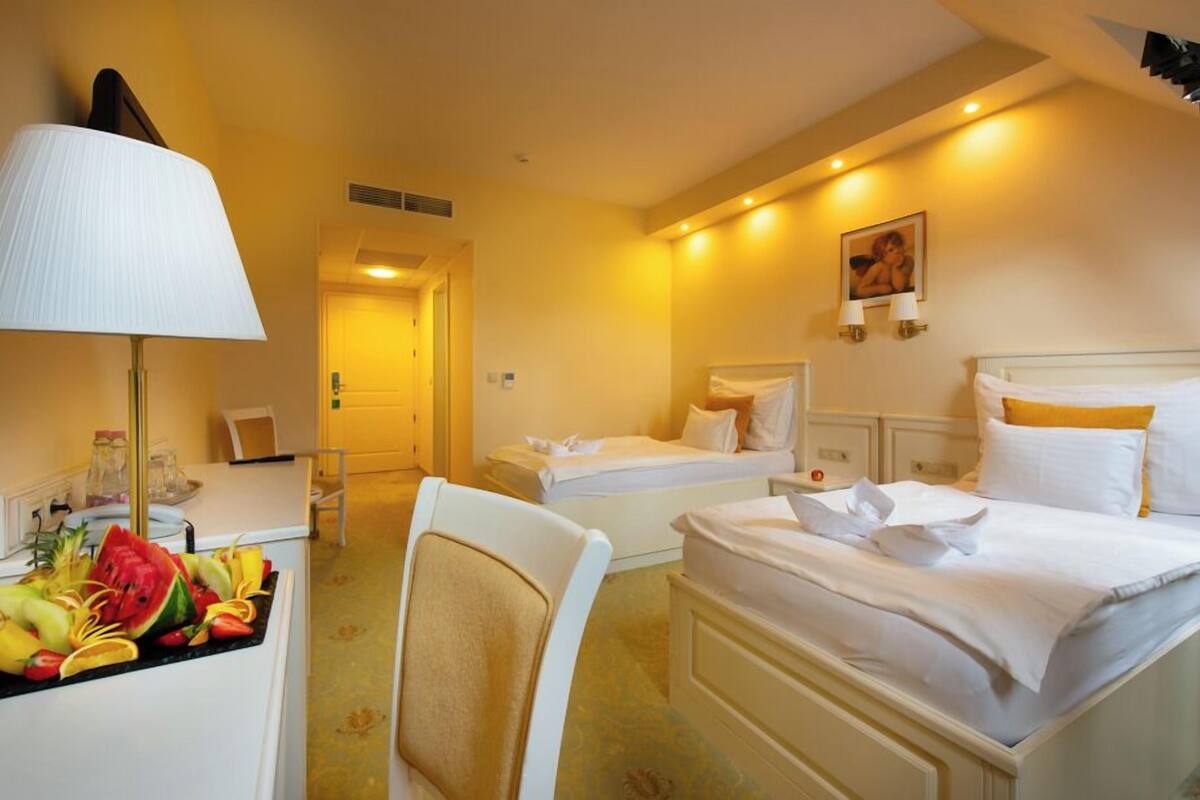 Quarto de hotel com duas camas, uma mesa com abajur e uma cesta de frutas.