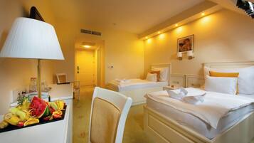 A hotel room with two beds, a desk with a lamp, and a fruit basket.