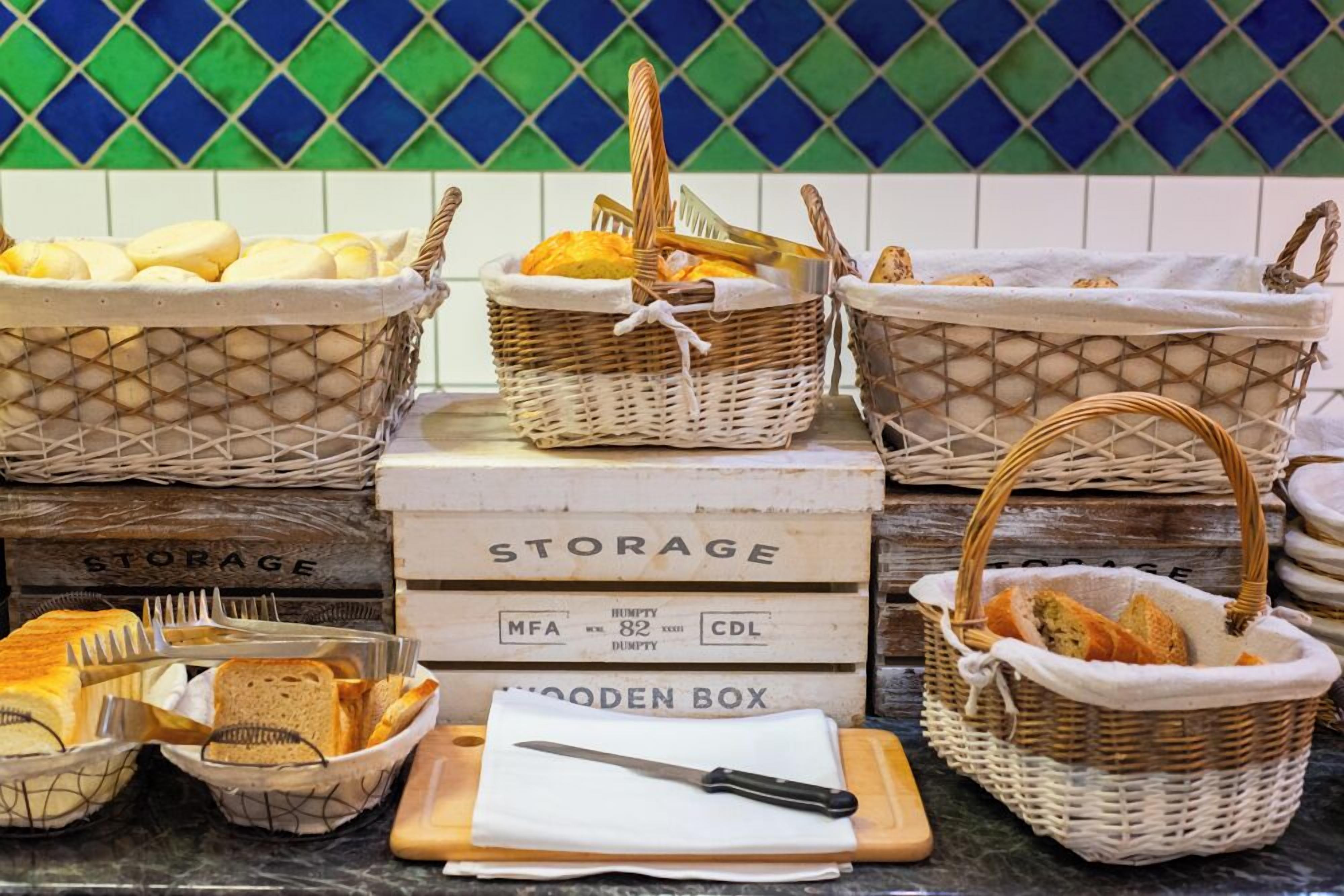 Una encimera de cocina con cestas variadas y un caja de madera con la etiqueta 'STORAGE' que contiene pan y utensilios.