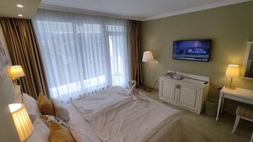 A hotel room with a large bed, a television on the wall, a desk with a lamp, and a window with curtains.