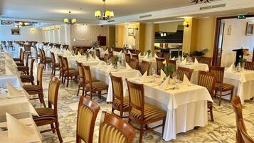 A banquet hall with long tables, wooden chairs, and chandeliers.