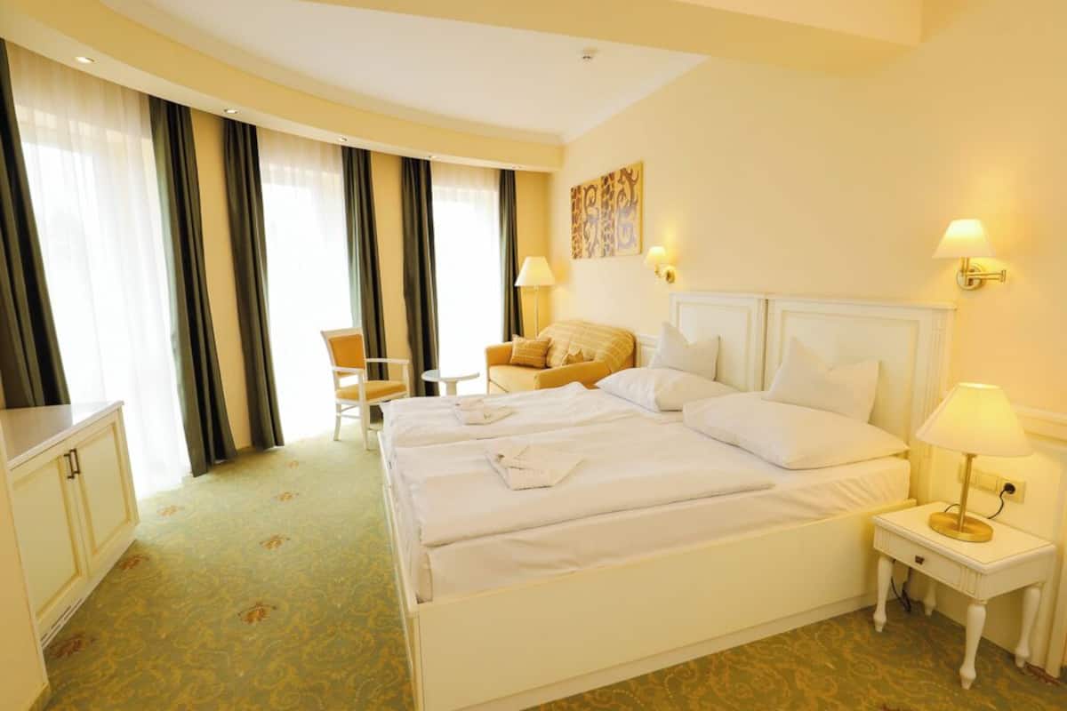 Quarto de hotel com duas camas, uma escrivaninha, uma cadeira e uma luminária.