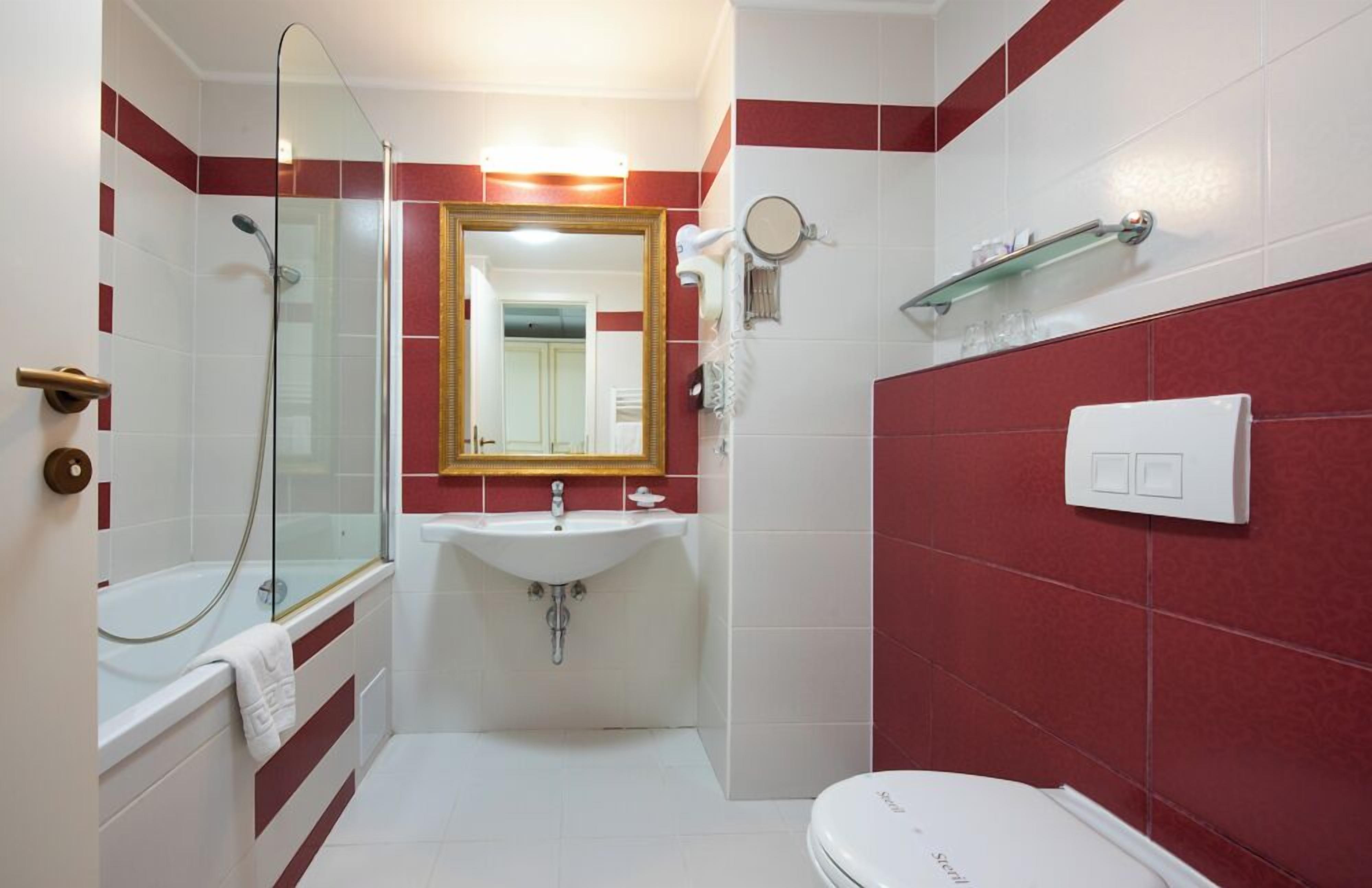 A bathroom with a glass-enclosed shower, a white sink, a mirror, and a toilet.