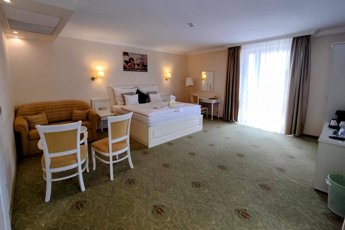 Quarto de hotel com cama, sofá, duas cadeiras, escrivaninha e janela com cortinas.