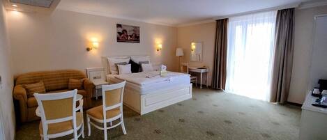 A hotel room with a bed, a sofa, two chairs, a desk, and a window with curtains.