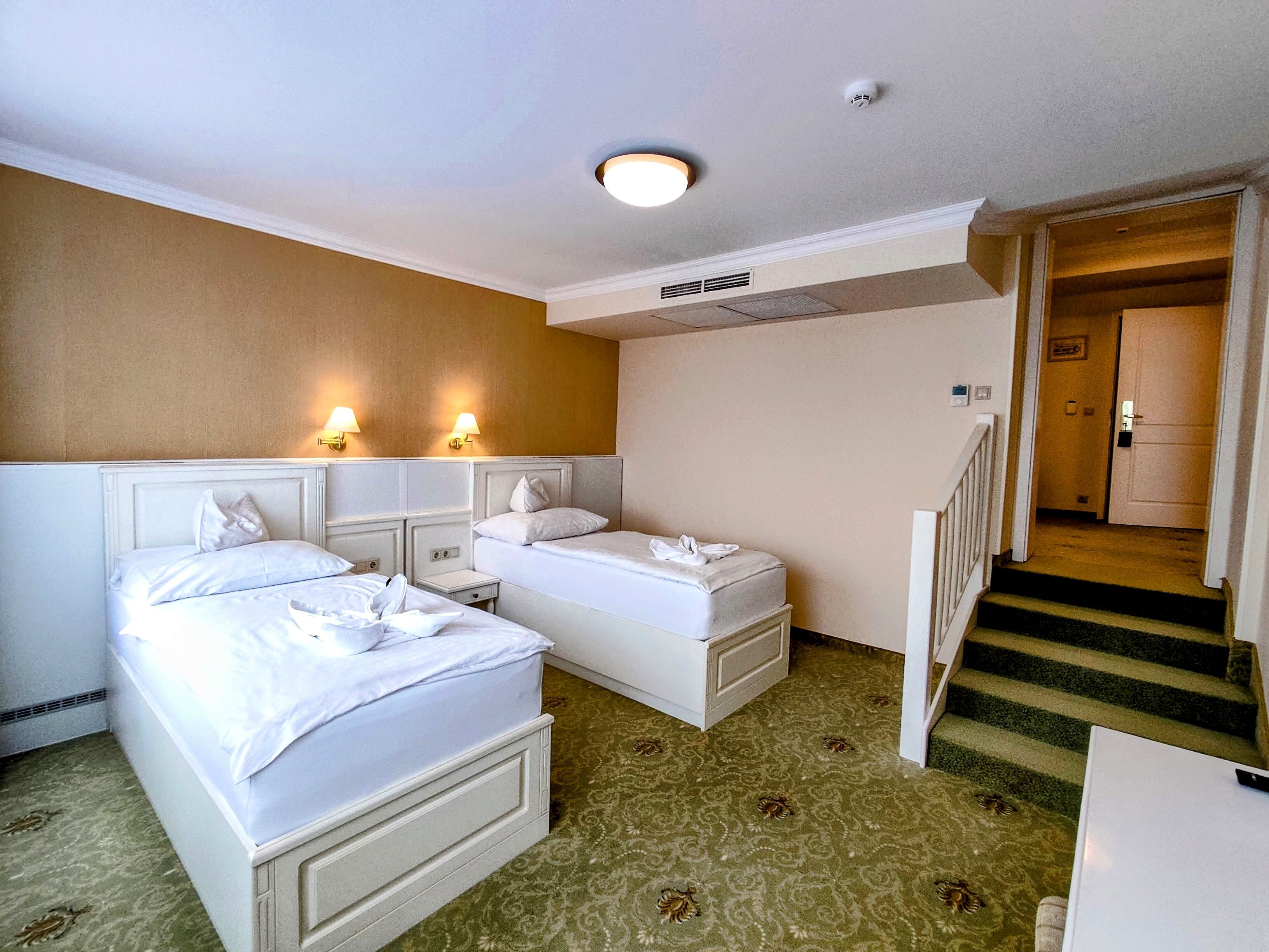 A hotel room with two beds, a staircase, and a door leading to another room.