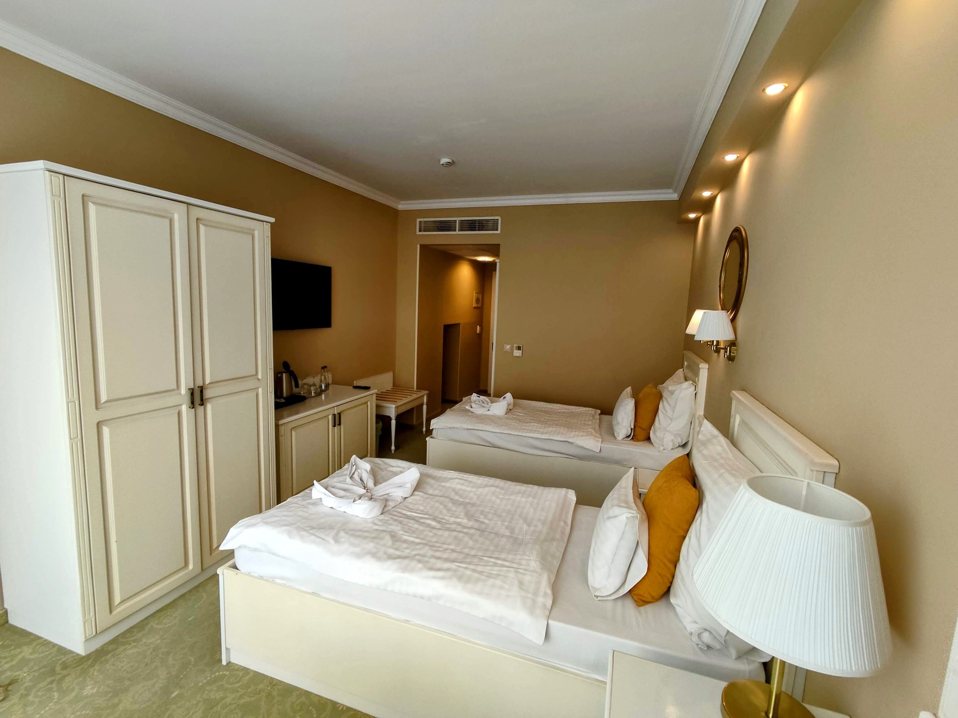 A hotel room with two beds, a wardrobe, a desk, and a television.