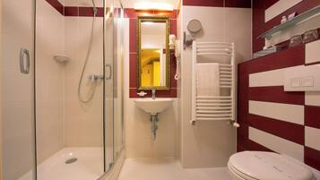 Un baño con ducha de vidrio, lavabo blanco, espejo, toallero y retrete.