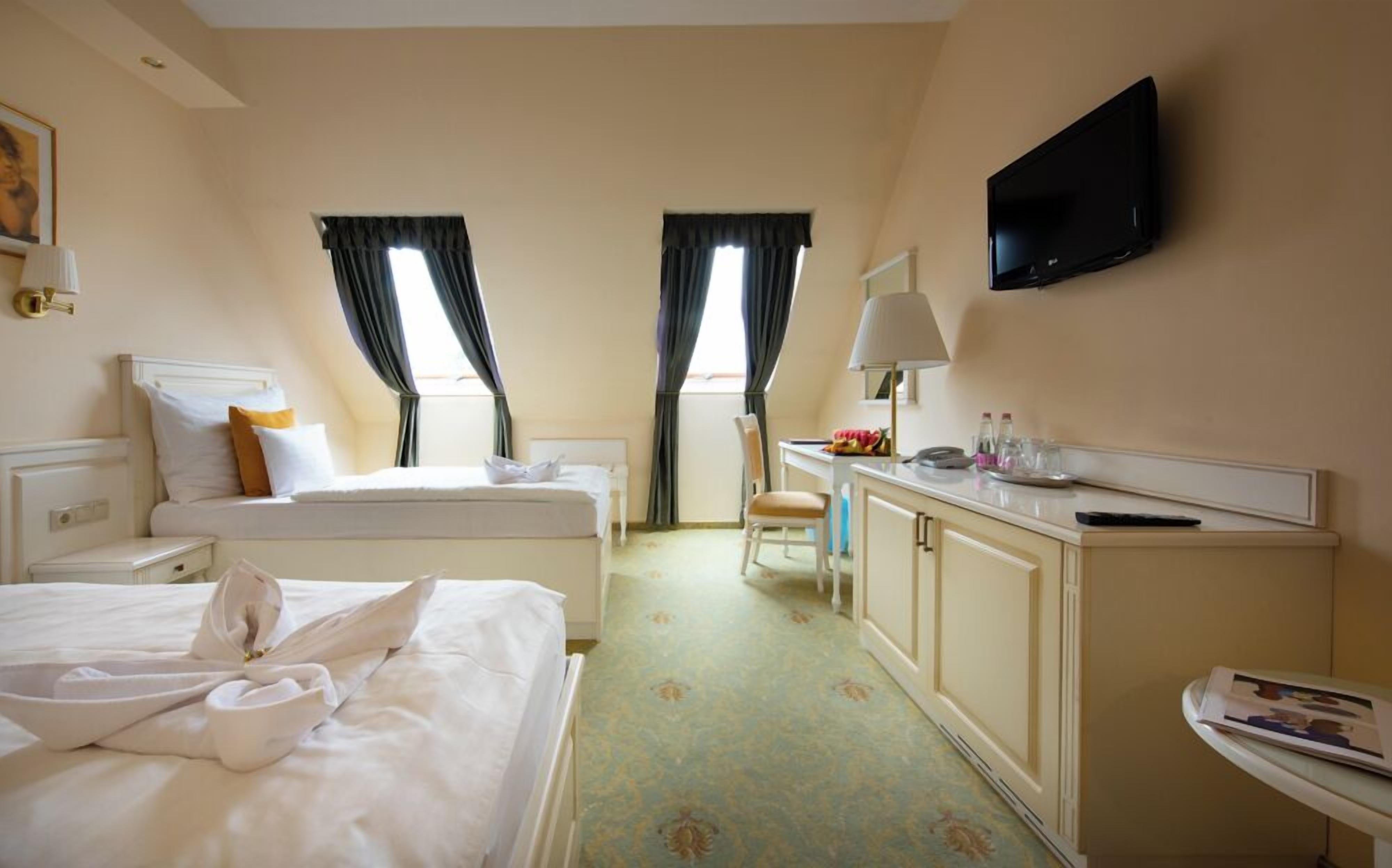 A hotel room with two beds, a desk, a TV, and a bathroom.