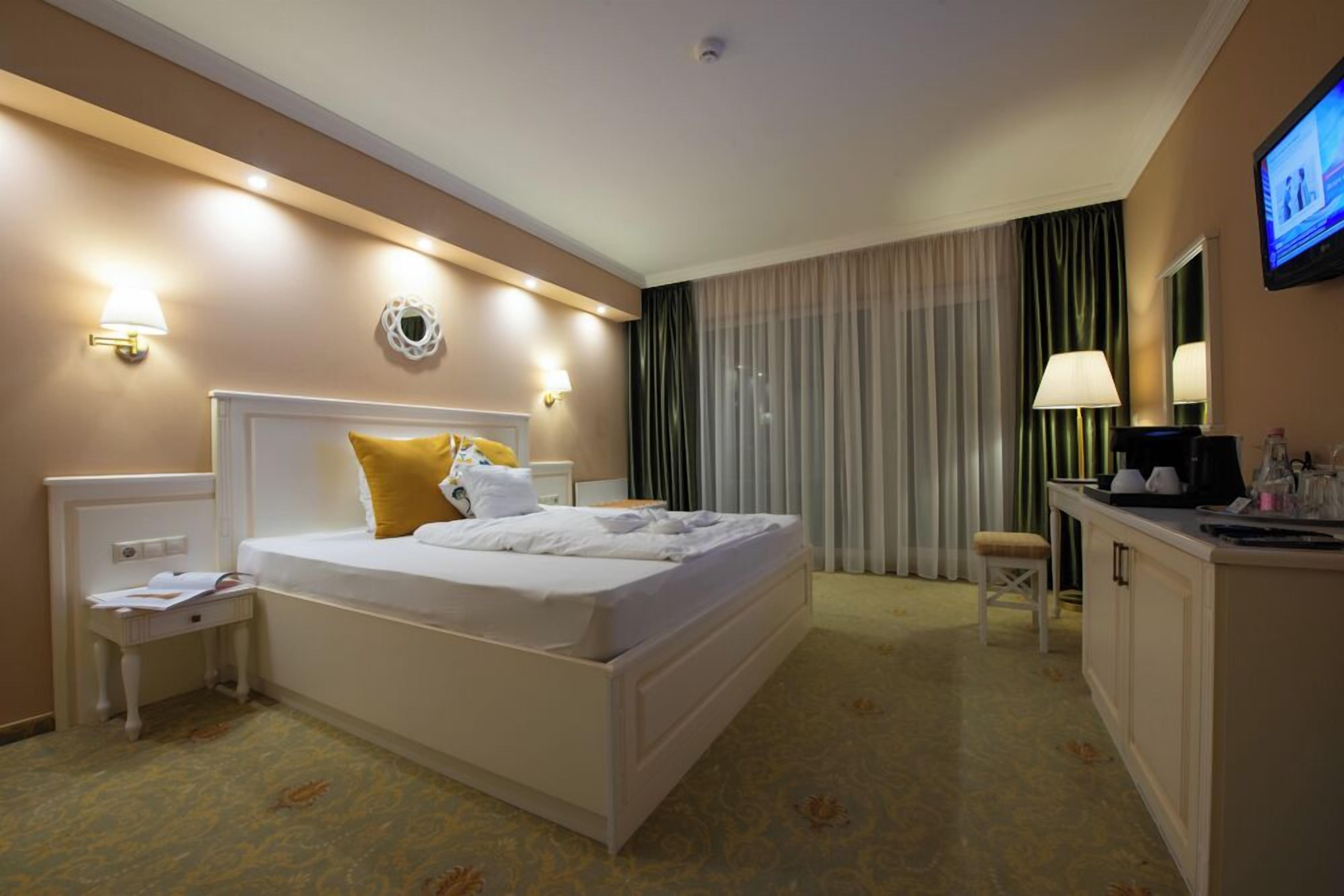 Ein Hotelzimmer mit Bett, Nachttischen, Schreibtisch, Stuhl, Fernseher und Vorhängen.
