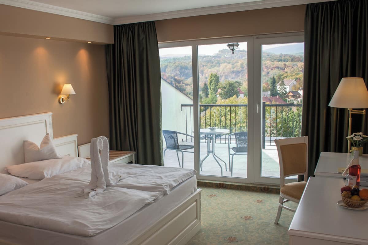 Quarto de hotel com cama, escrivaninha, cadeira, varanda com mesa e cadeiras, e vista para o exterior.