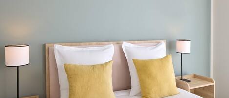 Una cama bien hecha con dos almohadas, un cabecero de madera y dos lámparas de noche sobre mesitas de madera.