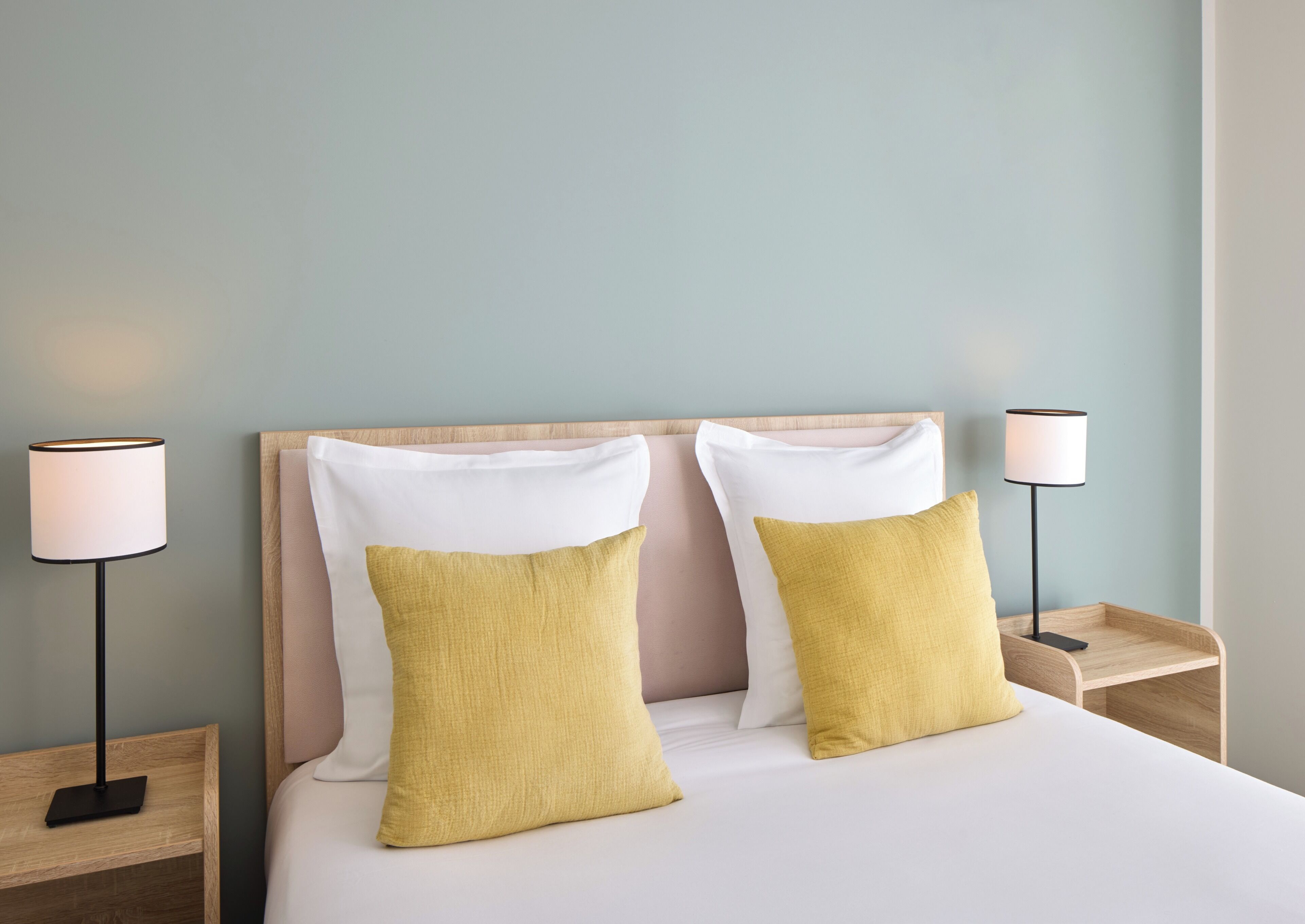 A neatly made bed with two pillows, a bedside lamp, and a wooden nightstand.