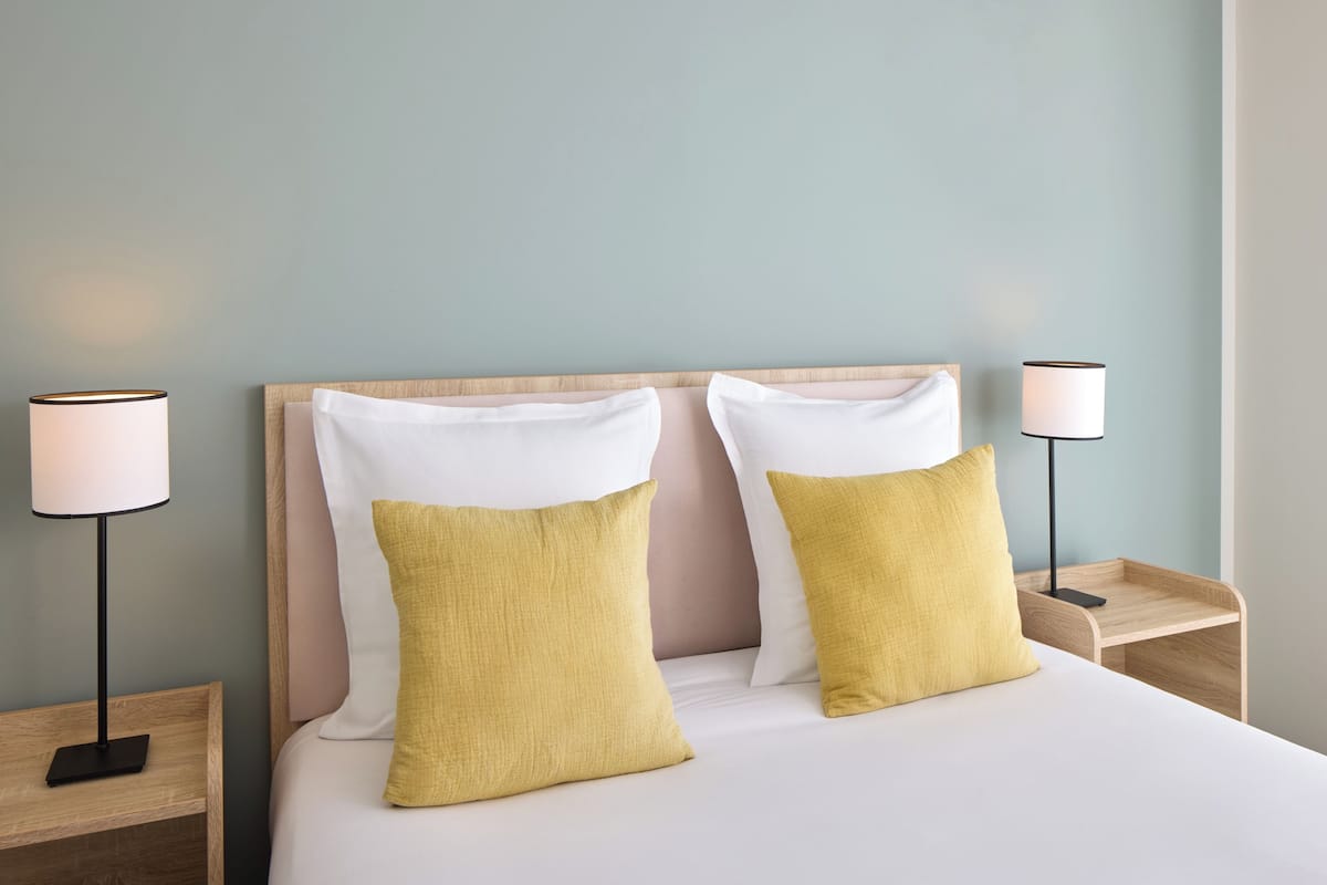 A neatly made bed with two pillows, a bedside lamp, and a wooden nightstand.