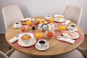 A round dining table with breakfast items including croissants, cereal, fruit, and beverages. - Quality Aparthotel Reims - Saint-Thomas (Reims)