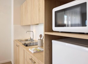 A modern kitchen with wooden cabinets, a stainless steel sink, a microwave, and a small appliance on the countertop. - Quality Aparthotel Reims - Saint-Thomas (Reims)
