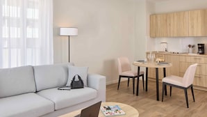 A modern living room with a sofa, a coffee table with a laptop and a magazine, a dining area with chairs and a table, and a kitchen with wooden cabinets and a sink. - Quality Aparthotel Reims - Saint-Thomas (Reims)