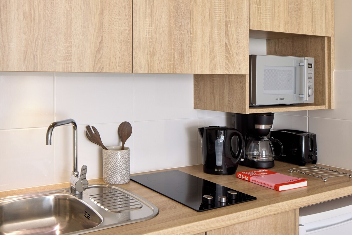 A modern kitchen with wooden cabinets, a stainless steel sink, a coffee maker, a microwave, and a tablet on the counter.