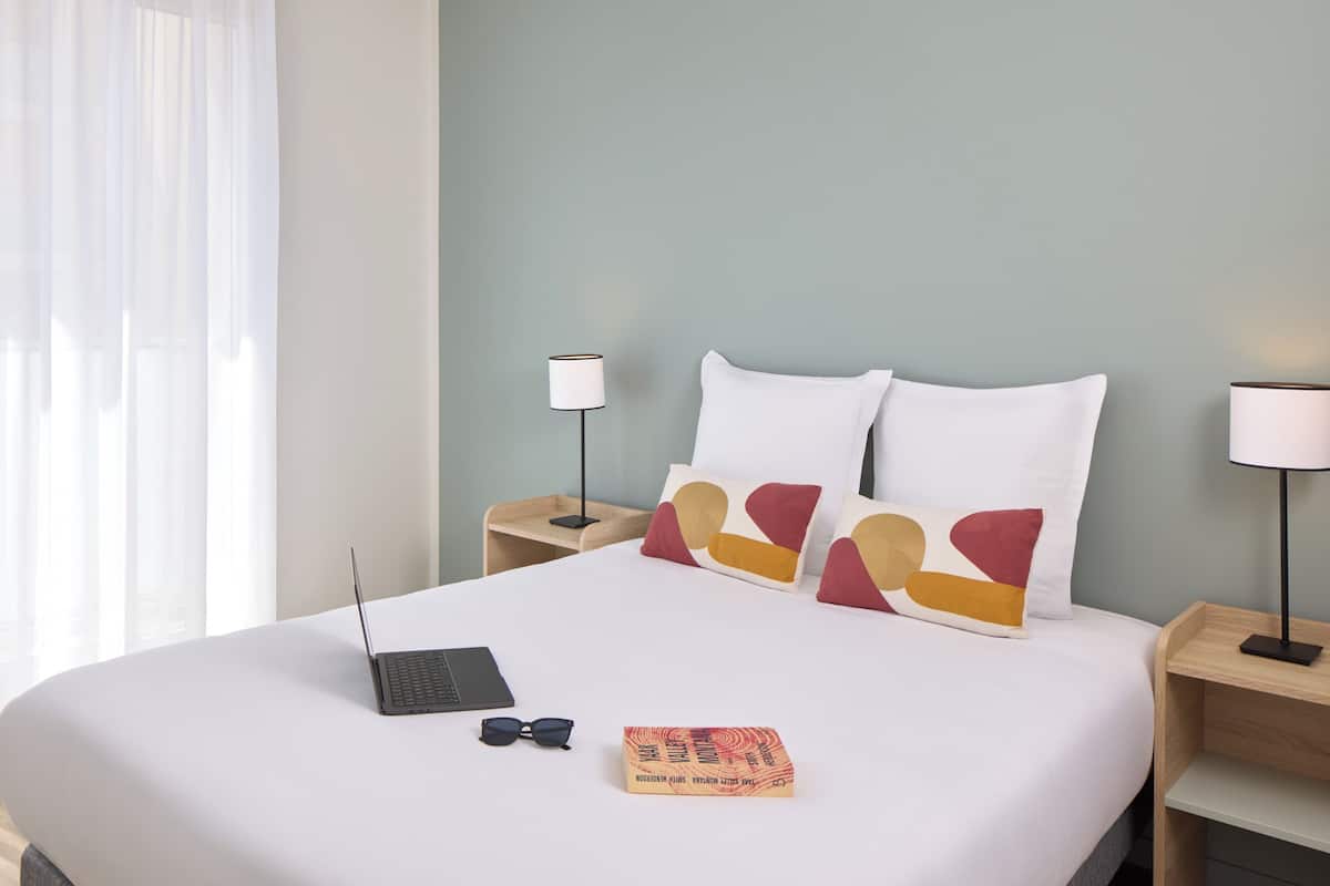 A neatly made bed with a laptop, glasses, and a book on the bed.