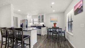 Une cuisine moderne avec des meubles blancs, un îlot central et un coin repas doté de chaises en bois foncé.