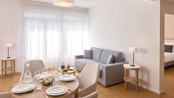 A modern living room with a grey sofa, a dining table set with plates and glasses, and a chandelier.
