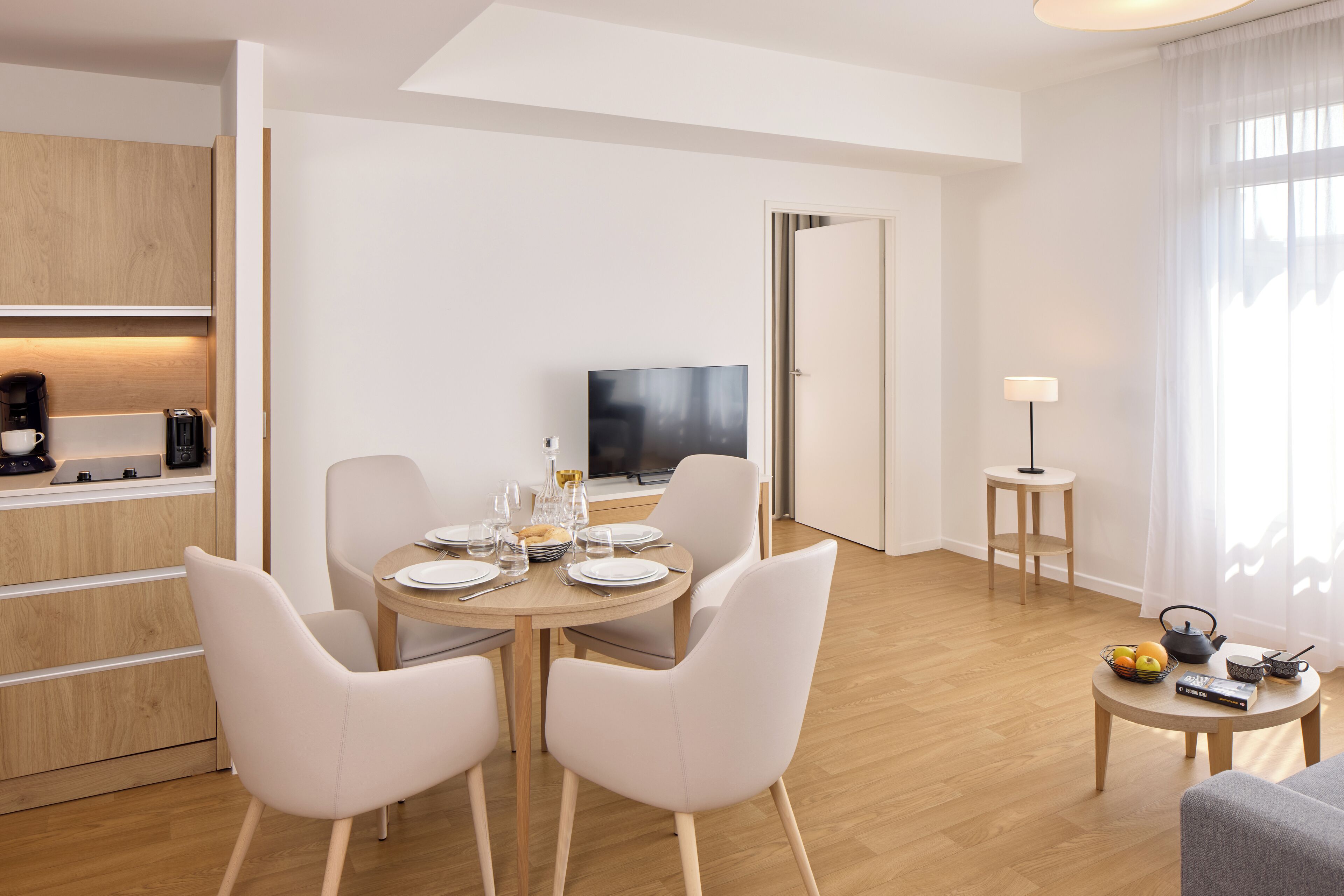 Une chambre d’hôtel moderne dotée d’un coin repas, d’une télévision et d’une petite table d’appoint avec une lampe.