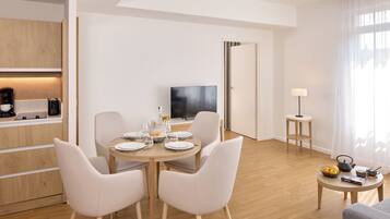 Une chambre d’hôtel moderne dotée d’un coin repas, d’une télévision et d’une petite table d’appoint avec une lampe.