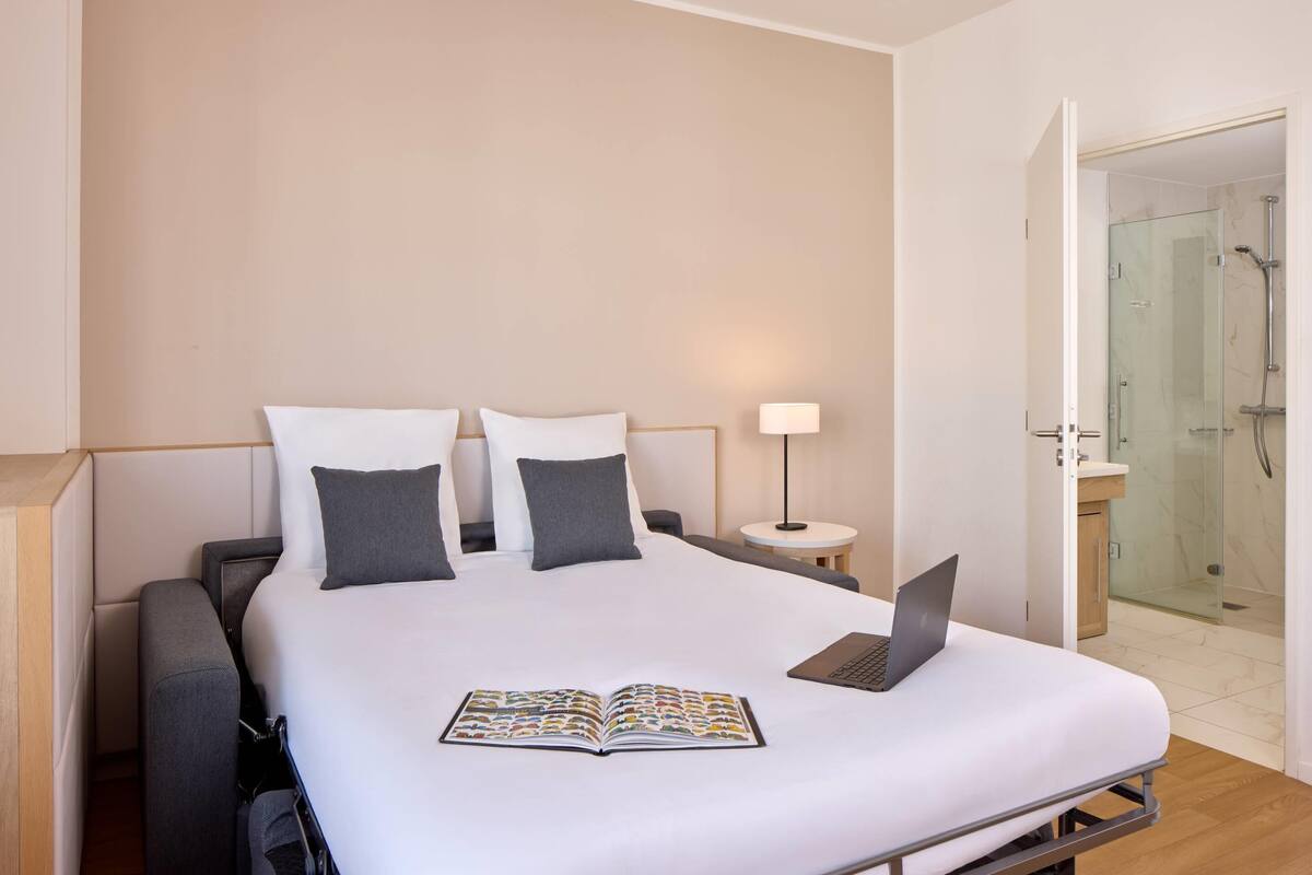 A modern hotel room with a large bed, a laptop, and a book on the bed.
