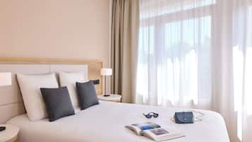 A hotel room with a large bed, a bedside table, a lamp, and a window with curtains.