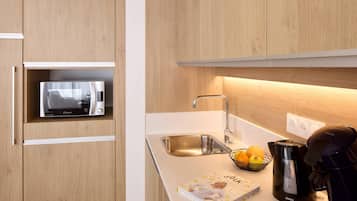 A modern kitchen with wooden cabinets, a built-in microwave, a sink, a coffee maker, and a fruit bowl.